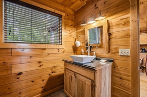 Step into your rustic retreats bathroom, where warm wood surrounds a sleek vessel sink and modern fixtures blend seamlessly with cabin charm. Natural light streams through windows, creating an inviti