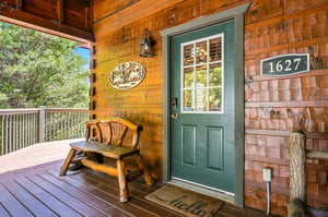 A warm welcome awaits at this charming cabin entrance, where rustic log accents and a handcrafted bench set the tone for your mountain retreat surrounded by nature.