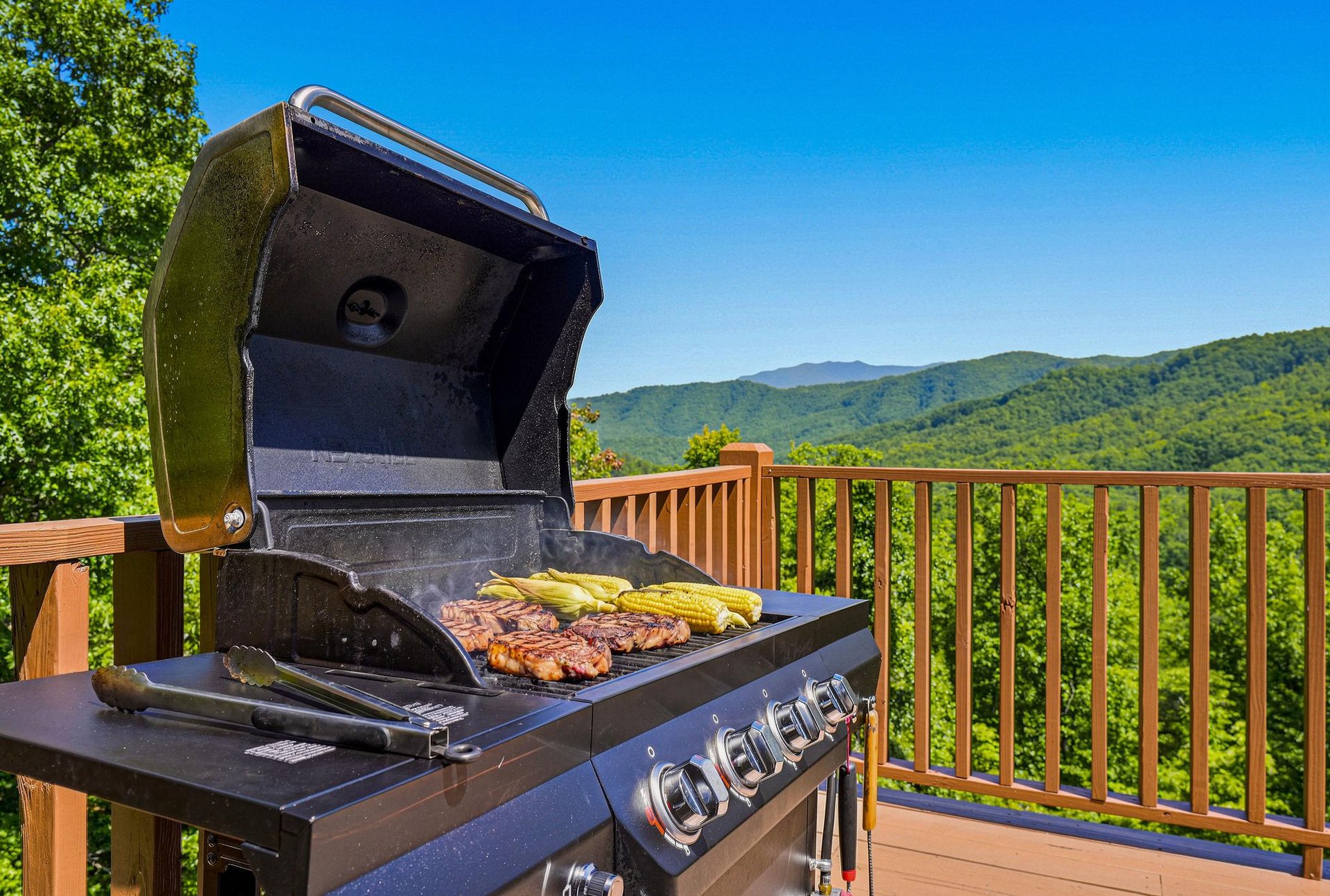 Sweeping mountain vistas frame your outdoor grilling space, where smoky BBQ and golden corn await under clear blue skies on your private deck.