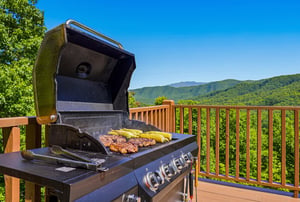 Sweeping mountain vistas frame your outdoor grilling space, where smoky BBQ and golden corn await under clear blue skies on your private deck.