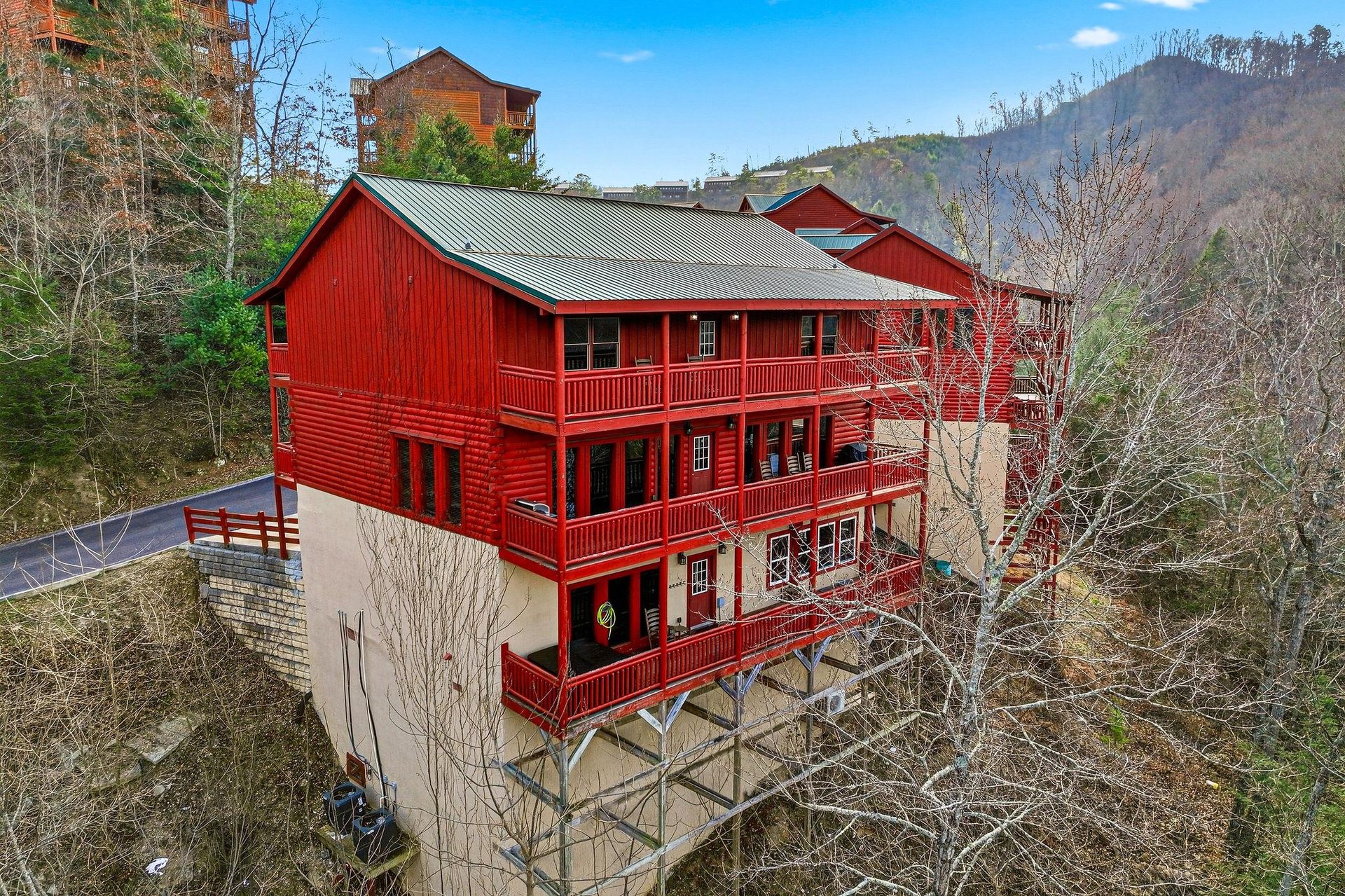 A striking red mountain cabin nestled among the hills, featuring multiple levels and spacious balconies with scenic mountain views.