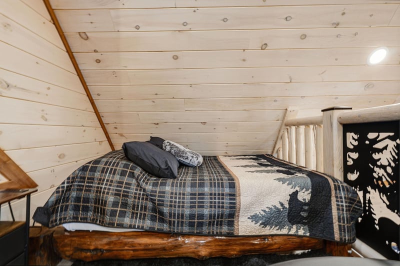 Cozy loft bedroom with rustic wooden beams and charming plaid bedding invites restful nights under slanted ceilings.