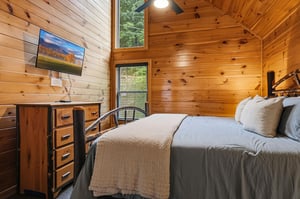Drift off in your cozy cabin bedroom, where warm wood surrounds you, high ceilings open the space, and treetop views peek through the windows—your peaceful retreat awaits.