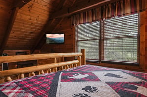 Settle into the cozy mountain lodge bedroom with its handcrafted log furnishings and vaulted wood ceiling. Natural light streams through large windows, while the charming quilt adds rustic warmth to 