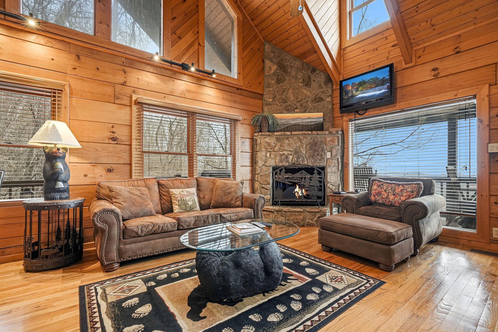 Relax in your spacious living room with soaring ceilings, stone fireplace, and panoramic windows bathing the warm wood walls in natural light.