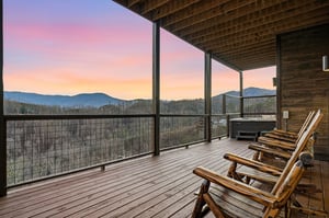 Covered deck featuring rustic log chairs and hot tub with breathtaking mountain views during sunset.