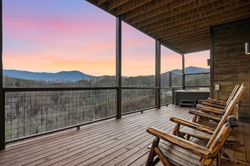 Covered deck featuring rustic log chairs and hot tub with breathtaking mountain views during sunset.