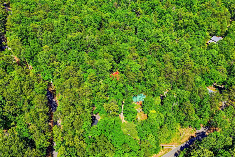 An aerial view showcasing the vacation rental property nestled within lush, vibrant forest, offering guests a secluded and natureimmersed retreat with winding paths and colorful rooftops peeking thro