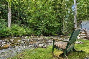 This peaceful creekside seating overlooks a gentle mountain stream surrounded by lush forest, offering a serene natural retreat perfect for relaxation and reflection.