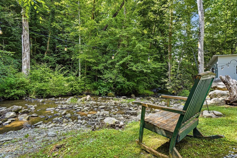 This peaceful creekside seating overlooks a gentle mountain stream surrounded by lush forest, offering a serene natural retreat perfect for relaxation and reflection.