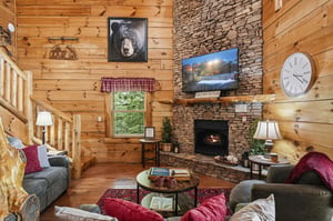 Cozy up in your inviting living room where rustic wood walls meet a stunning stone fireplace—perfect for unwinding after mountain adventures.