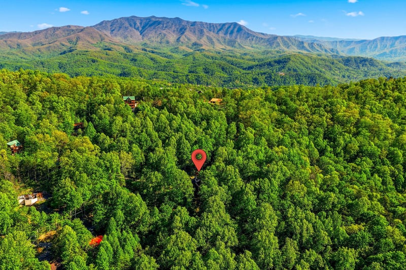 Aerial view showcases the propertys secluded location nestled among dense forests with stunning mountain ranges creating a dramatic backdrop.