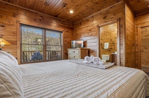Unwind in your cozy cabin bedroom with rustic wood paneling, crisp linens, and serene forest views framed by your window—perfect for a peaceful mountain retreat.