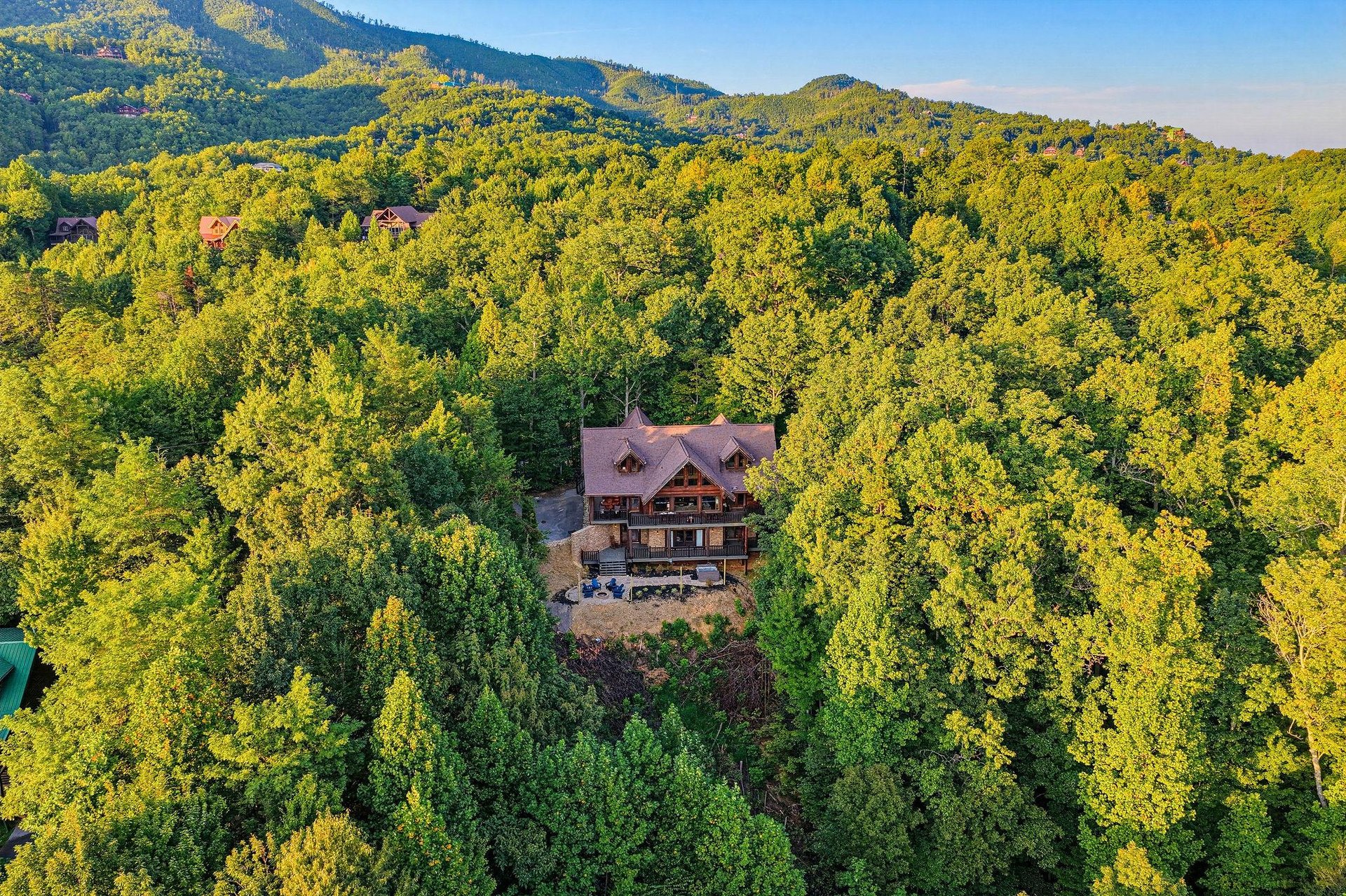 Aerial view of a secluded mountain lodge nestled among lush forest with stunning views of the surrounding peaks and natural landscape.
