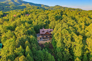 Aerial view of a secluded mountain lodge nestled among lush forest with stunning views of the surrounding peaks and natural landscape.