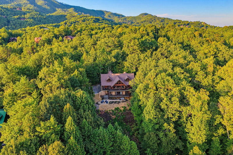 Aerial view of a secluded mountain lodge nestled among lush forest with stunning views of the surrounding peaks and natural landscape.