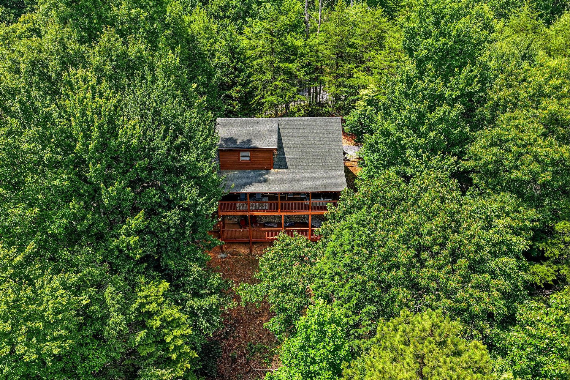 Aerial view of a secluded cabin with wraparound decks nestled among lush green forest, offering a private retreat in natures embrace.