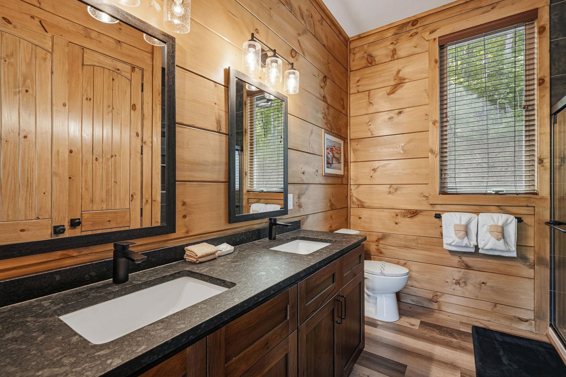 Unwind in your rustic bathroom featuring warm wood walls, granite counters, and thoughtful touches like fluffy towels awaiting your arrival.