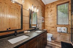 Unwind in your rustic bathroom featuring warm wood walls, granite counters, and thoughtful touches like fluffy towels awaiting your arrival.
