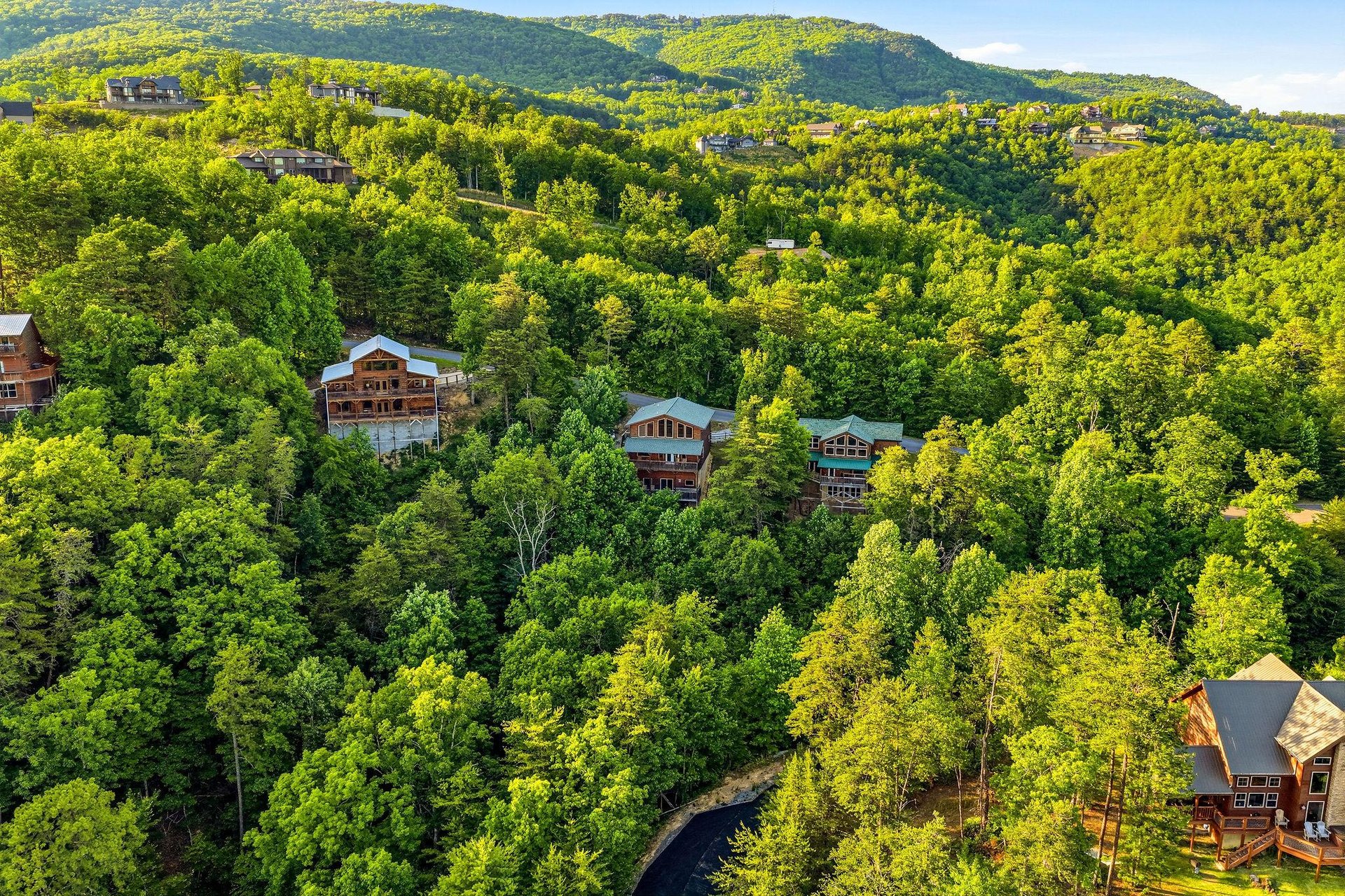 Aerial view of the vacation rental nestled among lush forested mountains, offering peaceful seclusion with neighboring properties visible in the scenic hillside community.