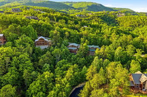 Aerial view of the vacation rental nestled among lush forested mountains, offering peaceful seclusion with neighboring properties visible in the scenic hillside community.