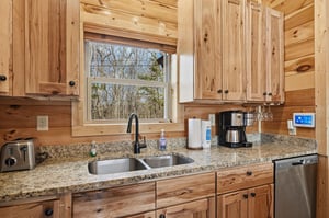 Your fully equipped kitchen features rustic wood cabinets, granite counters, and forest views while you brew morning coffee.