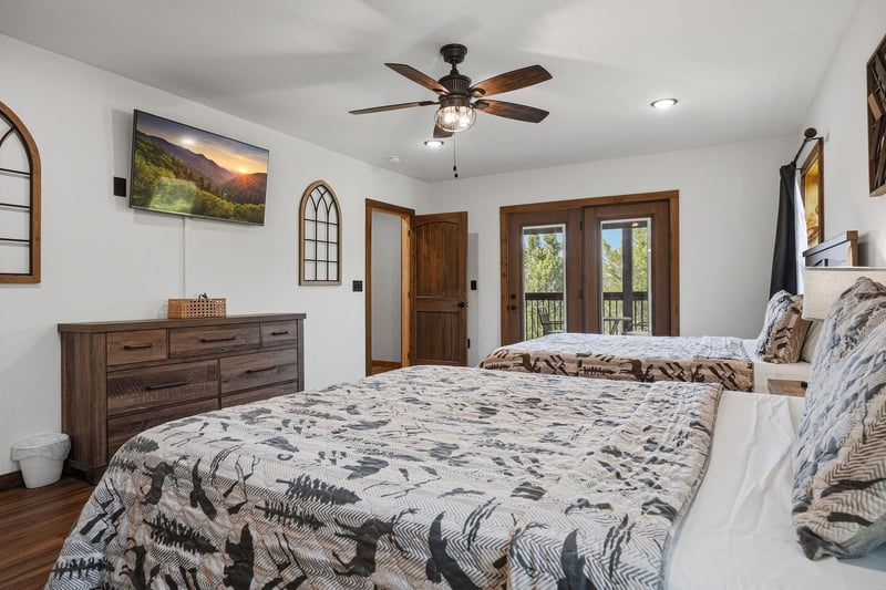 Step into your bright, airy retreat with two comfy beds, warm wood accents, and a welcoming fan overhead. French doors open to a private balcony—your perfect escape.