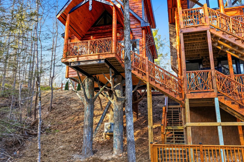 Rustic treehouse cabin elevated among towering trees, featuring multiple wooden decks and stairways for a unique forest retreat experience.