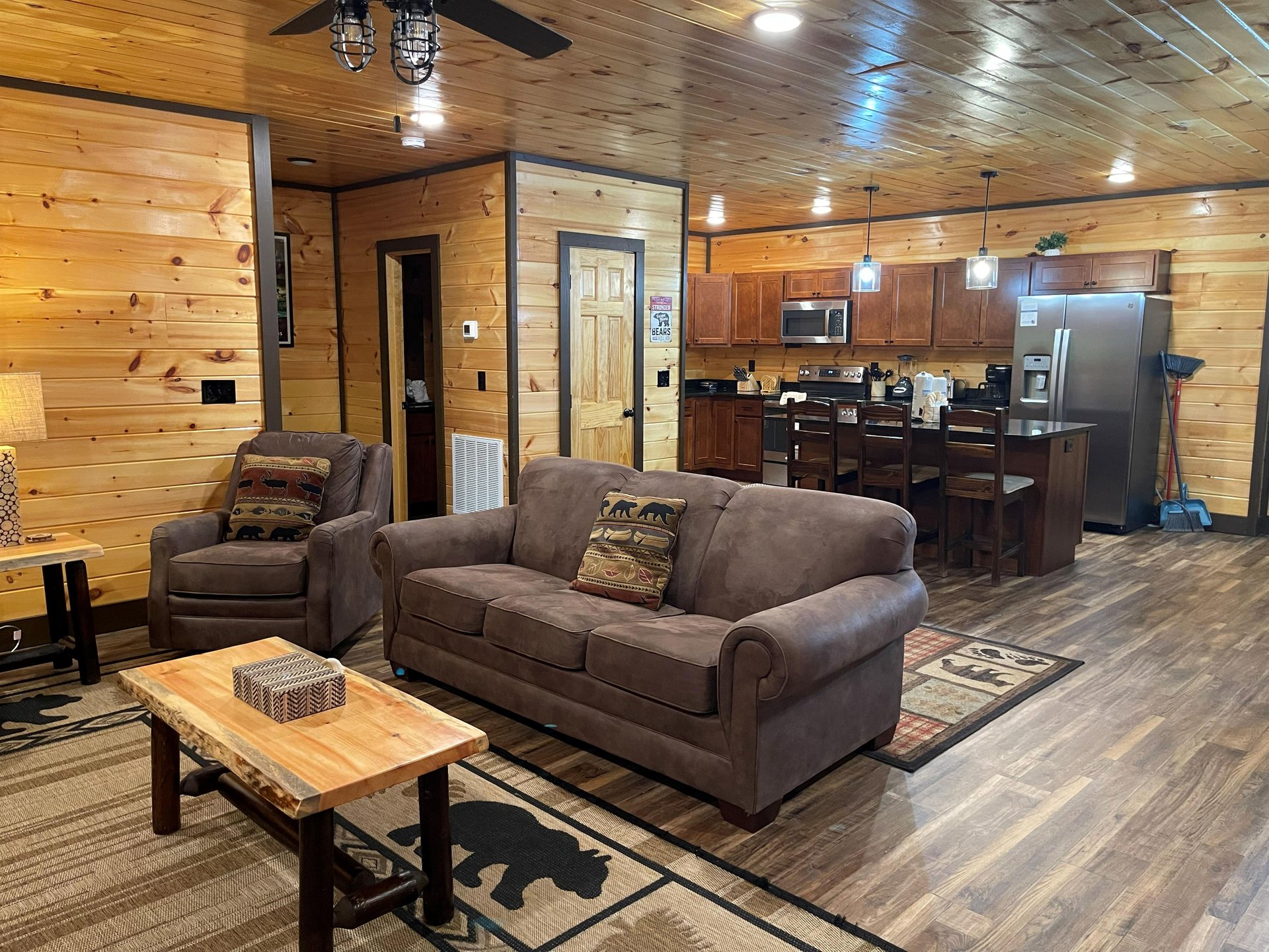 Settle into your cozy cabin retreat with rustic pine walls and plush seating in the living room, flowing seamlessly to your full kitchen with modern appliances and a breakfast bar—perfect for gatherin