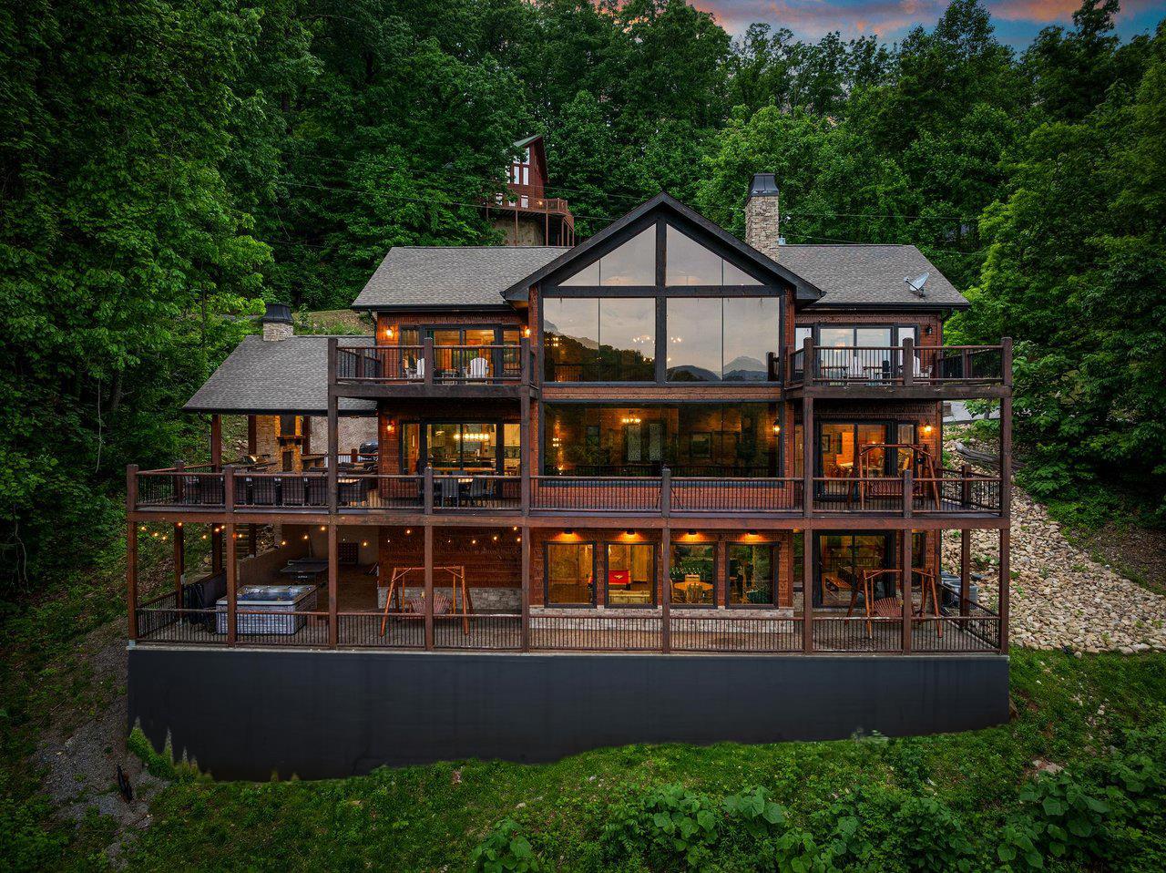 Stunning lakefront cabin showcases warm lights against lush forest backdrop during golden hour.