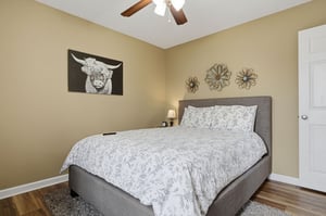 Sink into your plush gray bed dressed in soft floral linens, where a gentle ceiling fan and charming artwork create a peaceful retreat for restful nights.