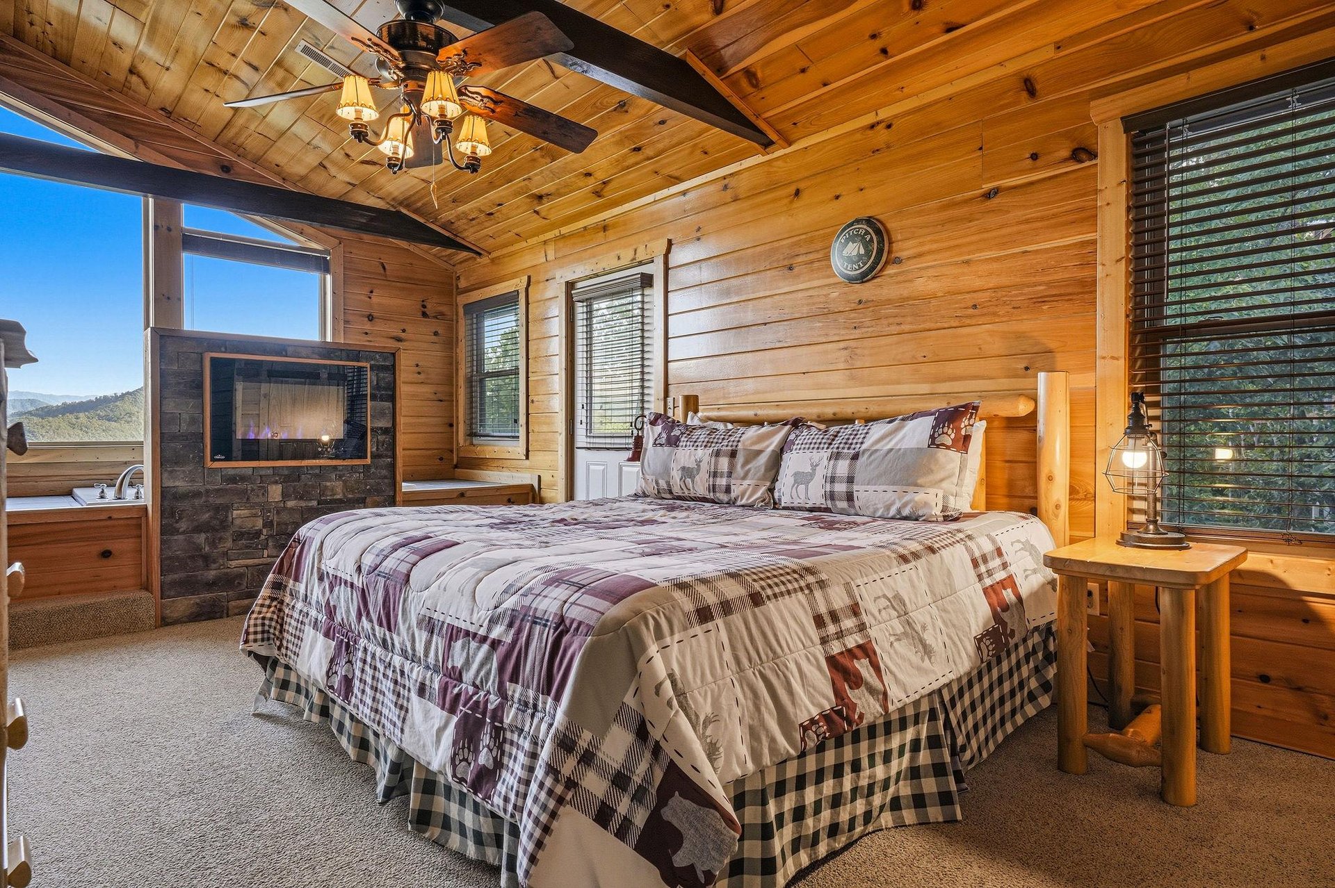 Relax in your cozy cabin bedroom with vaulted wood ceilings, a plush bed, a warm fireplace, and mountain views through large windows. The perfect retreat after exploring the area.