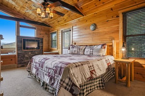 Relax in your cozy cabin bedroom with vaulted wood ceilings, a plush bed, a warm fireplace, and mountain views through large windows. The perfect retreat after exploring the area.