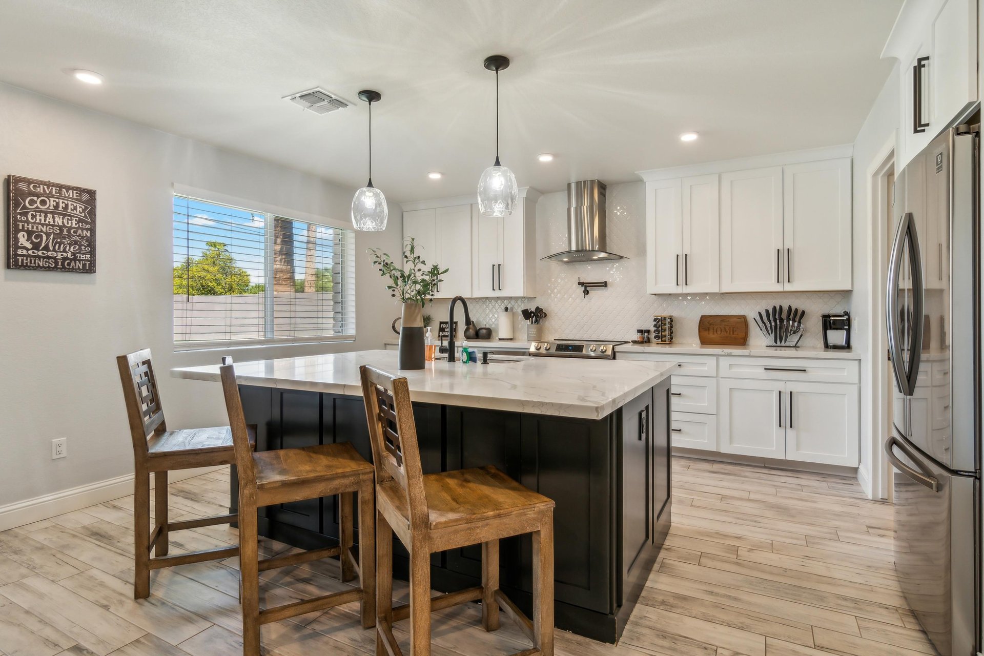 The kitchen features a spacious island with a white marble countertop and a black base, surrounded by wooden chairs with a rustic finish.