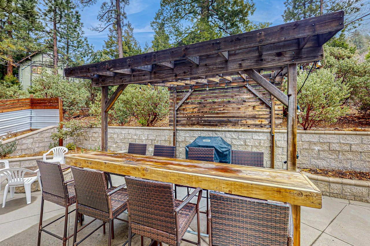 This rustic wood bar seats 8 under a covered pergola, with a builtin BBQ grill right nearby — an ideal spot for outdoor dining and entertaining.