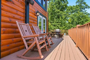 Sunlit deck with handcrafted rocking chairs frames your peaceful forest retreat, where mornings unfold with birdsong and coffee among the trees.