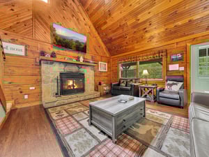 Relax in your cozy cabin living room, where warm wood walls and crackling fireplace create perfect mountain retreat vibes.