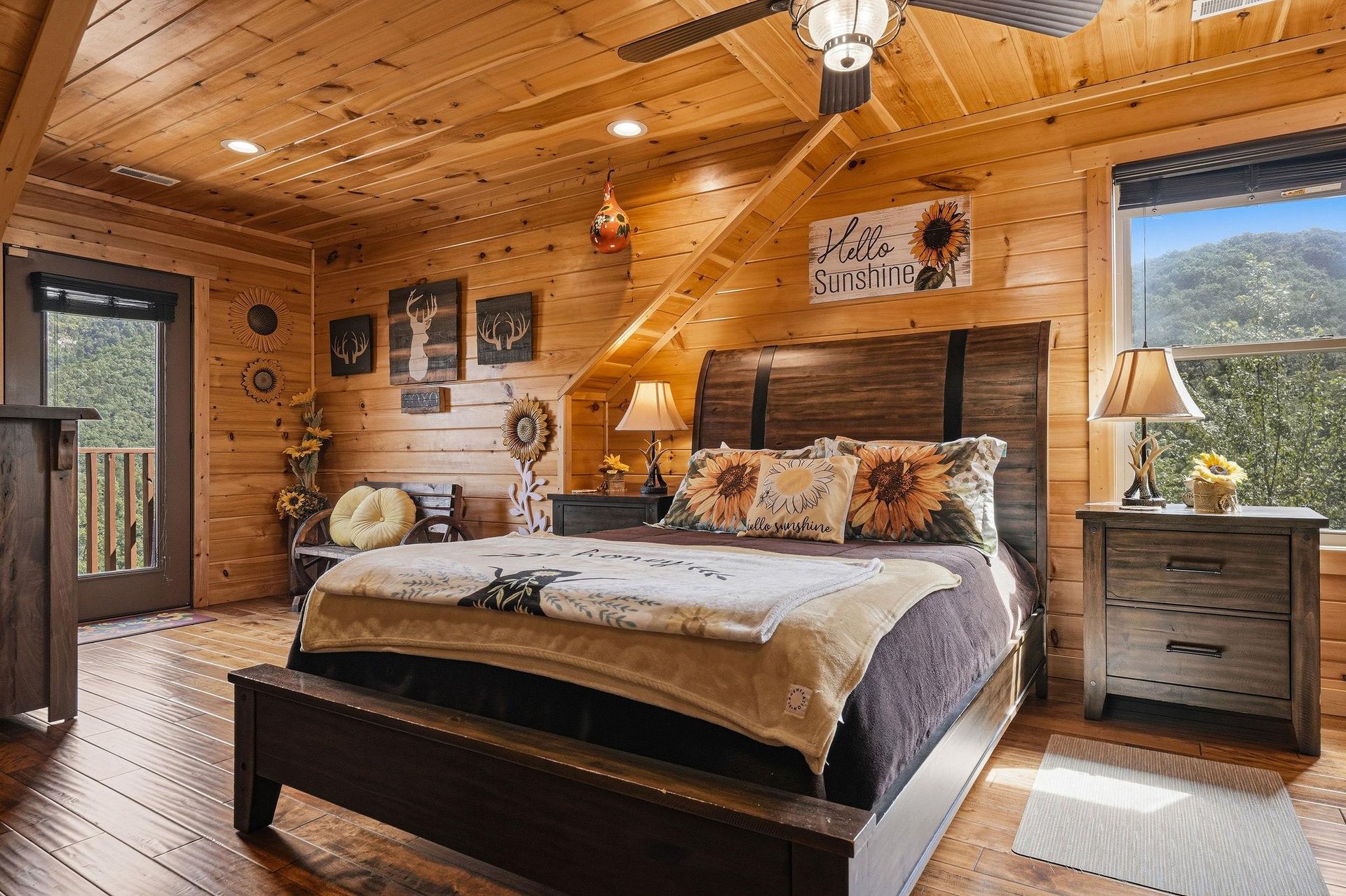 Drift off in your cozy loft bedroom, wrapped in rustic wood and sunflower charm, with sunlight streaming through large windows framing peaceful mountain views.