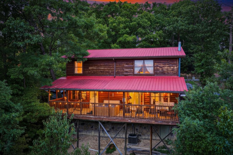 Rustic cabin with a welcoming glow nestled among lush trees beneath a vibrant sunset sky.