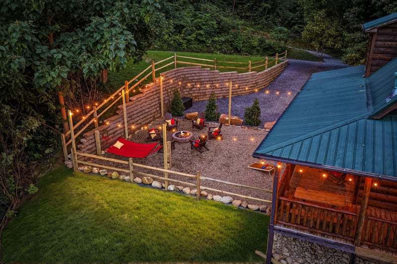 Aerial view of the property featuring a cozy fire pit patio surrounded by natural hillside greenery and warm ambient lighting at dusk.