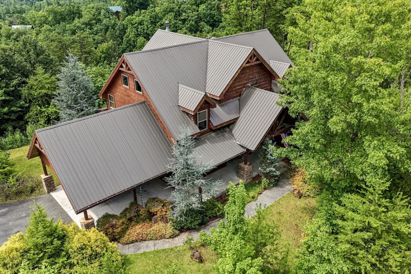 A spacious mountain cabin nestled in lush forest surroundings, featuring beautiful natural wood siding and a modern metal roof. The property offers peaceful seclusion with mature trees and landscaped 