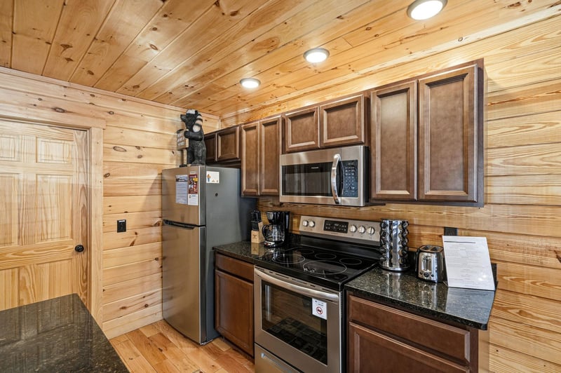 Your fully equipped kitchen features rich wood cabinets, granite counters, and modern appliances in a cozy log cabin setting.