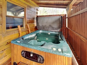 Your private hot tub awaits on the covered deck, surrounded by natural wood and peaceful forest views—perfect for unwinding after a day of adventure.
