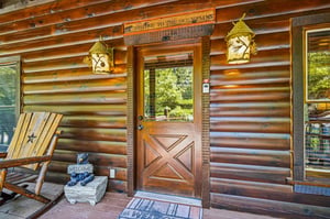 The rustic log cabin entrance features warm wooden details, charming decorative lanterns, and a welcoming bear figurine that sets the tone for a cozy mountain retreat. This inviting facade promises th