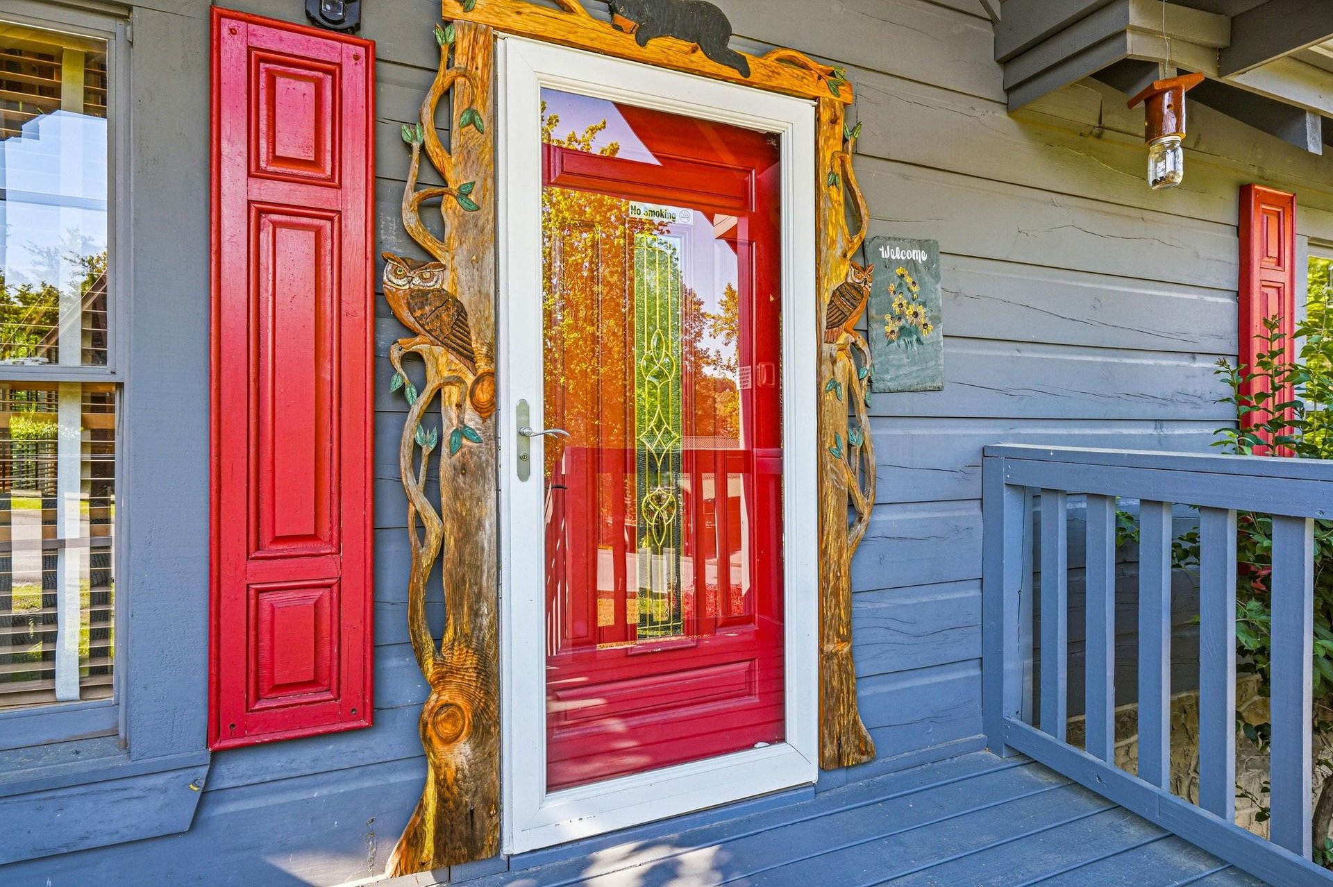 Charming entrance with vibrant red door and artistic wooden tree frame welcomes visitors to this unique property.