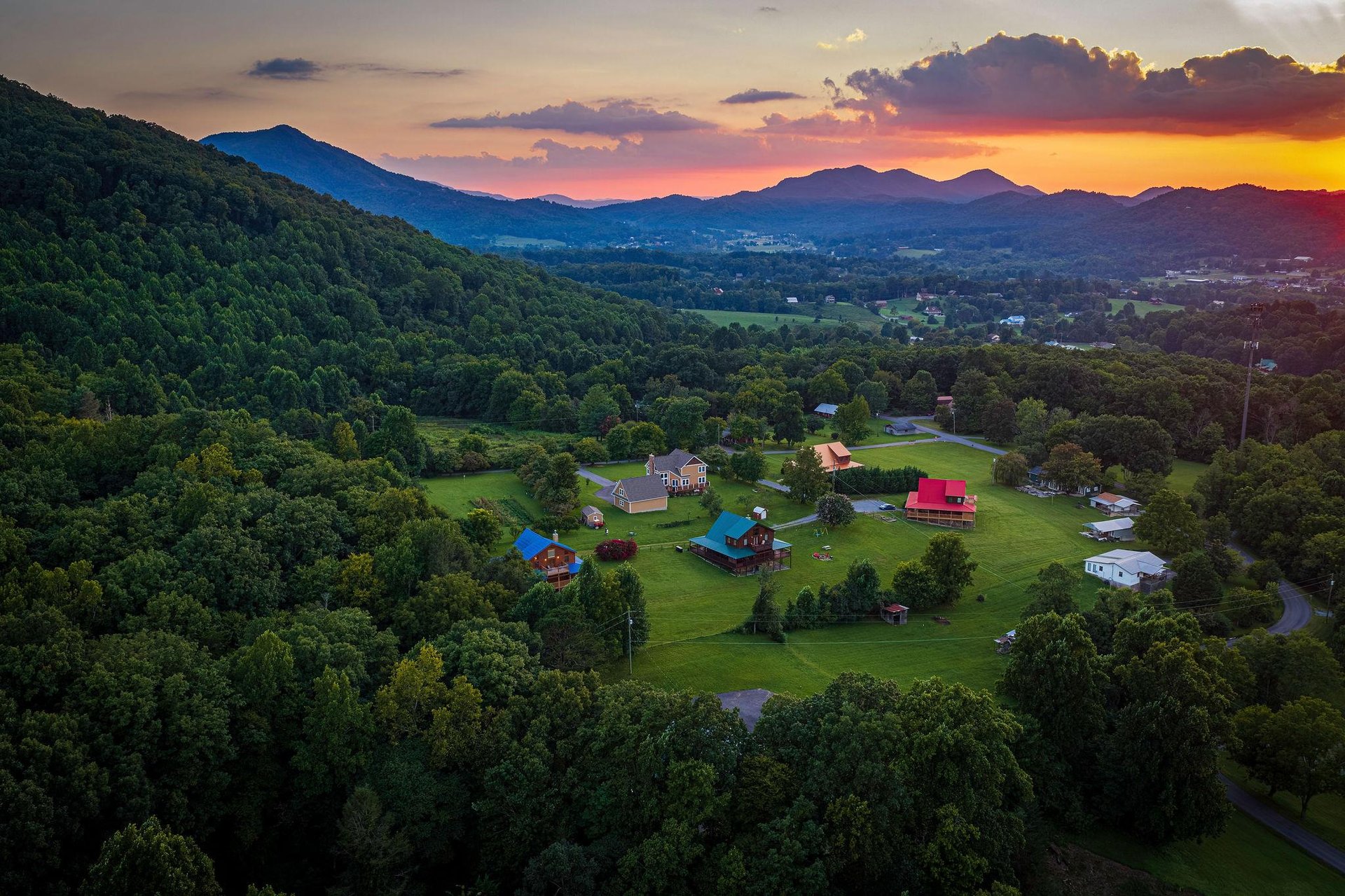 Aerial view of the property nestled in a lush valley, framed by rolling mountains and vibrant sunset skies.