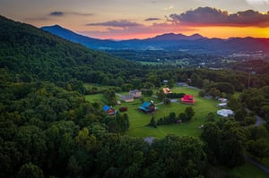 Aerial view of the property nestled in a lush valley, framed by rolling mountains and vibrant sunset skies.
