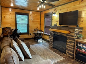 Relax in your rustic living room with a cozy stone fireplace, ceiling fan, and comfortable seating. Board games and natural wood finishes invite you to unwind.