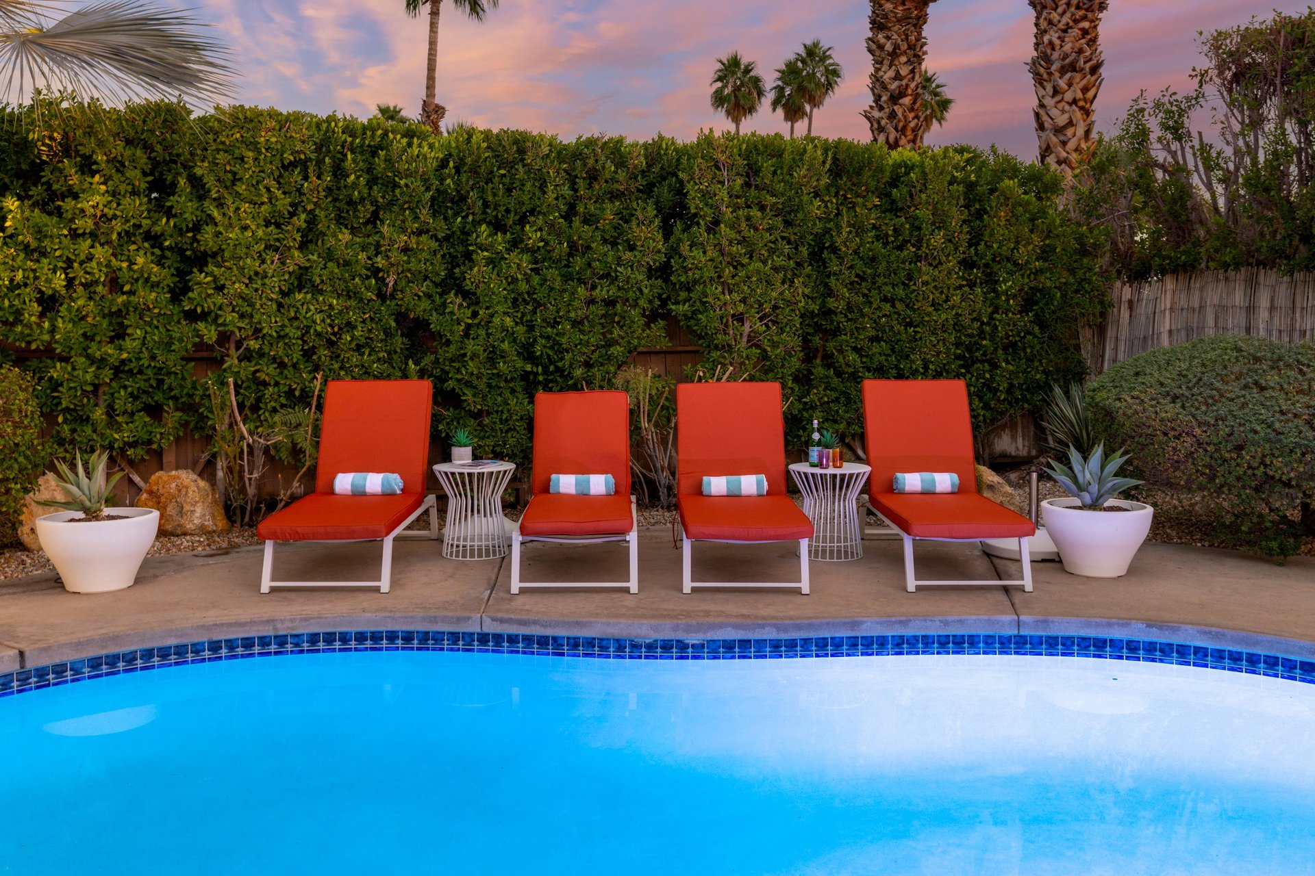 Unwind poolside on vibrant orange loungers as desert palms frame stunning twilight skies above your private oasis.