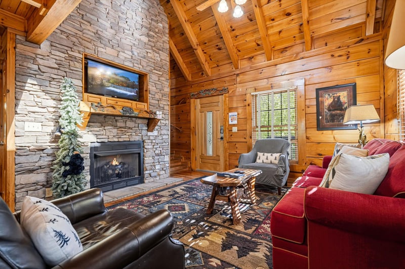 Relax in your rustic living room featuring exposed beams, stone fireplace, and cozy seating that creates the perfect cabin retreat.